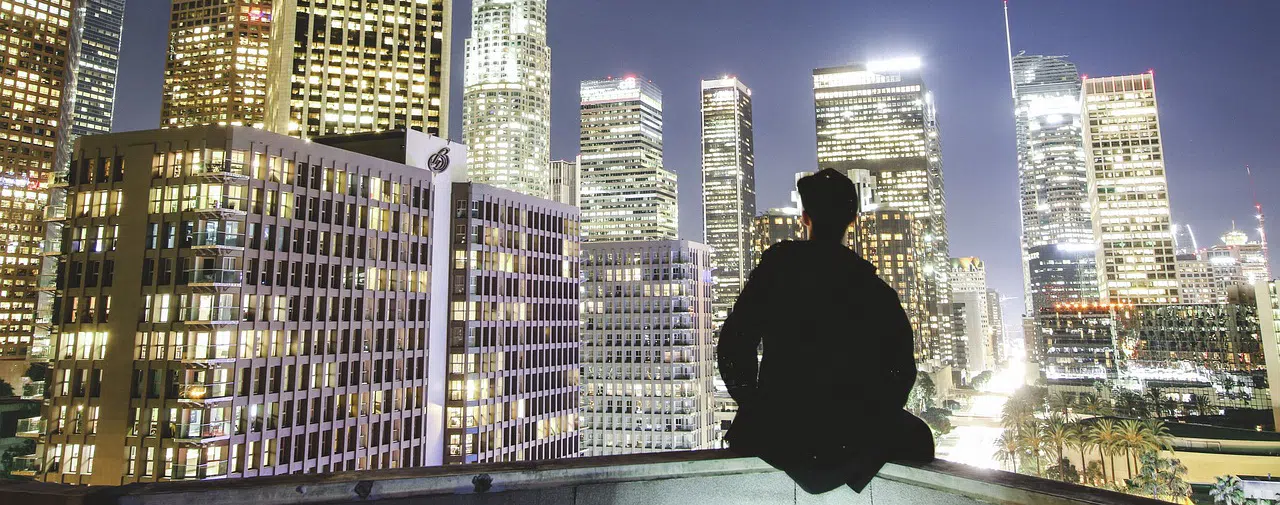 male sitting on balcony edge overlooking skyline at night